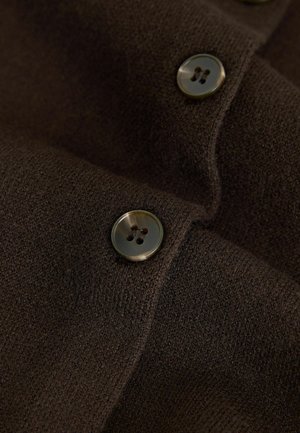 Brauner Stoff mit einer glatten Textur, der zwei runde, dunkle Knöpfe mit vier Löchern zeigt, die teilweise übereinander liegen.