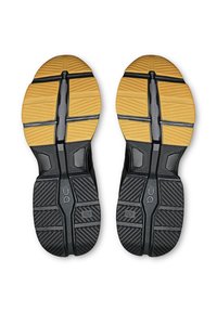 Semelles de chaussures de sport noires et jaunes avec un motif texturé ; présentent des rainures et des sections prononcées pour une traction et une flexibilité.