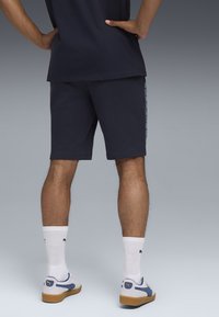 Marineblå shorts med lige snit, foret sideakcenter, båret med hvide sokker og sneakers med blå detaljer. Glat stofstruktur observeret.