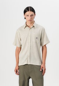 Kortermet, beige skjorte med vertikale striper, knapping foran og en brystlomme med et lite brodert design.