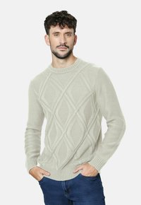 Suéter de punto gris claro con un patrón de diamante, cuello redondo y puños acanalados. Combinado con jeans azules.
