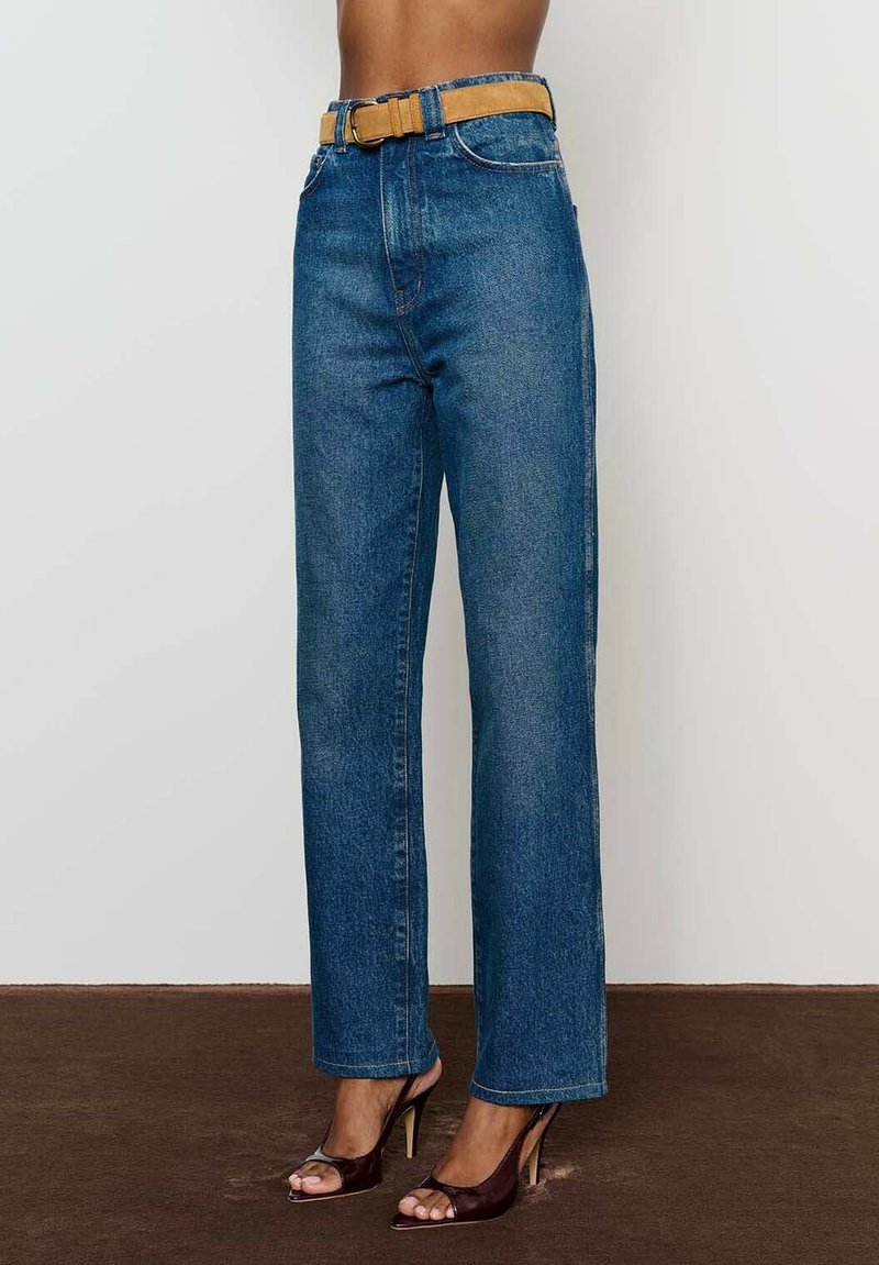 Aukštu liemeniu mėlyni džinsai su tiesia forma, su kontrastinga smėlio spalvos diržu ir siuvimo detalėmis ant kišenių.