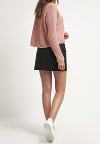 Hellrosa gestrickter, cropped Pullover mit strukturiertem Muster, kombiniert mit einem schwarzen Minirock. Die Model trägt weiße Sneakers.