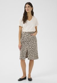 Beige panterprint rok met een split aan de voorkant, gemaakt van katoen, gecombineerd met een crèmekleurige V-hals T-shirt. Zwarte platte schoenen maken de look compleet.