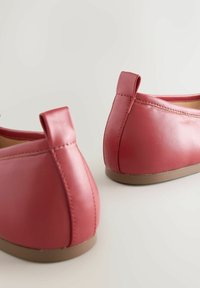 Pantofi slip-on din piele roșie, cu textură netedă, formă rotunjită și toc mic. Partea din spate are un detaliu cu buclă pentru a-i pune ușor.