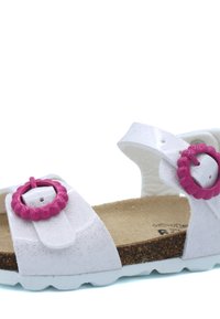 Sandale blanche scintillante avec deux boucles circulaires roses, semelle intérieure douce et semelle texturée. Le design présente des brides larges et une ouverture au niveau des orteils.