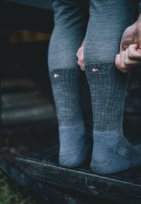 Calcetines gruesos de lana gris con un diseño acanalado, que presentan un detalle en rojo en la parte superior y suelas acolchadas en gris, proporcionando calor y comodidad.