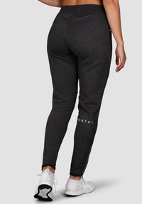 Gray sweatpants with a slim fit, elastic waistband, side zipper accents, and white branding on the lower leg, paired with white sneakers.