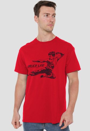 Red cotton t-shirt featuring a black graphic print of Bruce Lee in a martial arts pose. Short sleeves and a crew neckline.