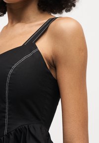 Κοντινό πλάνο ενός ατόμου που φοράει μαύρο αμάνικο τοπ με λευκές ραφές στο λουρί και στην περιοχή του στήθους.