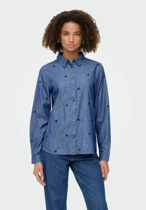 Donkerblauw denimshirt met lange mouwen, kraag en knopen aan de voorkant. Voorzien van kleine, hartvormige borduursels in marineblauw verspreid over de stof.