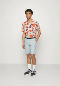 Chemise à manches courtes avec un imprimé floral orange et bleu, associée à un short bleu clair, des chaussettes blanches et des baskets marines.
