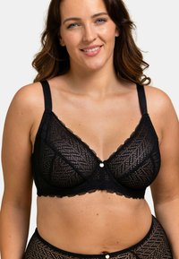 Soutien-gorge en dentelle noire avec un motif géométrique, bretelles ajustables et un petit accent métallique au centre. Tissu souple et texturé.
