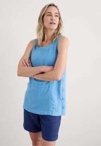 Světle modrý top bez rukávů s kulatým výstřihem, texturovaná látka a boční knoflíky. Kombinováno s námořnickými šortkami s ohrnutými manžetami.