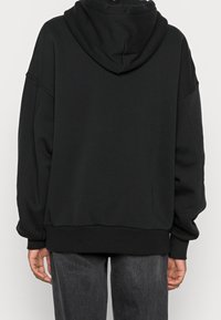 Felpa nera con cappuccio in morbido tessuto, taglio oversize, polsini e orlo a coste, con una grande tasca e design minimalista.