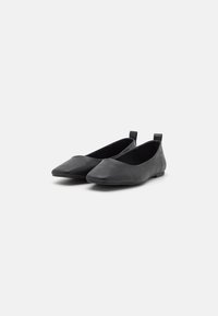 Bailarinas ortopédicas pretas em couro com um design de bico fino, forma minimalista e pequenos puxadores de calcanhar para facilitar o calce. Textura suave, sem hardware visível.
