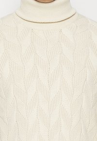 Cremefarbener Rollkragenpullover mit einem strukturierten Strickmuster im Fischgräten-design, präsentiert mit einem gerippten Kragen und Bündchen.