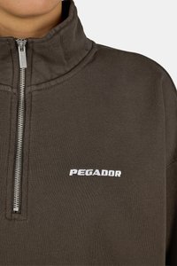 Ciemnobrązowa bluza z zamkiem błyskawicznym z wysokim kołnierzem, przemysłowym zamkiem i białym logo "PEGADOR" na piersi, wykonana z miękkiego materiału.