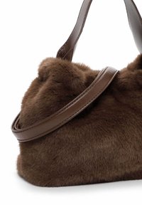 Brown faux fur handbag with a rounded shape. Features a smooth brown leather strap and soft, textured surface. No visible hardware details.
