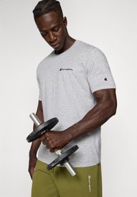 Grå bomulds t-shirt med broderet "Champion" logo, rund halsudskæring og korte ærmer, sammen med olivengrønne bukser.