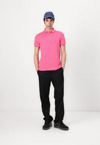 Rosa polo t-shirt med vit och röd randig krage, bärs med svarta byxor och svarta sneakers. Avslappnad keps i blått tyg.