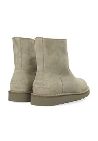 Beige suède enkellaarsjes met platte rubberen zolen en zichtbare stiksels, weergegeven vanuit de achterkant en iets opzij.