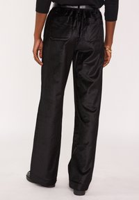 Pantalon noir à jambes larges en tissu doux et lisse, avec une taille haute, des poches arrière, et une coupe décontractée. Surface texturée avec un léger éclat subtil.
