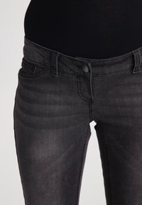 Jeans de mezclilla negra con un corte ajustado, que cuentan con un cierre de botón, cinco bolsillos y un leve desgaste en la textura de la tela.