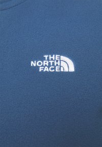 Niebieska bluza polarowa z fakturowanej tkaniny, z okrągłym dekoltem oraz haftowanym białym logo "The North Face" z zakrzywionym łukiem.