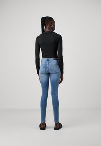 Fekete hosszú ujjú felső világoskék skinny farmernadrággal párosítva. A farmernadrágon két hátsó zseb található és enyh�én kopott hatású. Fekete szandál van rajta.