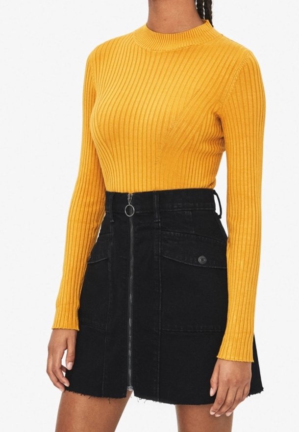 Haut à manches longues en ribbed moutarde associé à une jupe en denim noire avec une fermeture éclair à l'avant et deux poches latérales, détail d'ourlet effiloché.