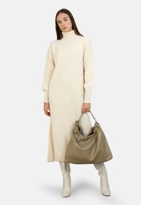 Vestido suéter de cuello alto color crema con mangas largas, combinado con un bolso verde oliva holgado y botas de rodilla blancas brillantes.