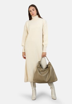 Cream-colored turtleneck sweater dress with long sleeves, paired with a slouchy olive green handbag and glossy white knee-high boots.