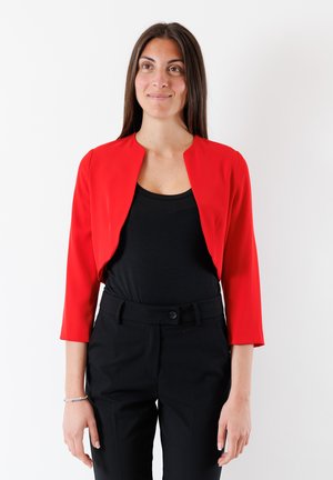 Blazer rosso, corto, con maniche a tre quarti, con texture liscia; indossato sopra una maglia nera e abbinato a pantaloni neri. Design del colletto semplice.