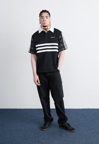 Black polo shirt with white stripes, featuring plaid sleeves. Paired with black jeans and black shoes, on a blue carpet background.