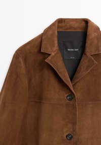 Bruine suède jas met een kraag, knoopsluiting en twee horizontale naden. Label toont het merk "Massimo Dutti".