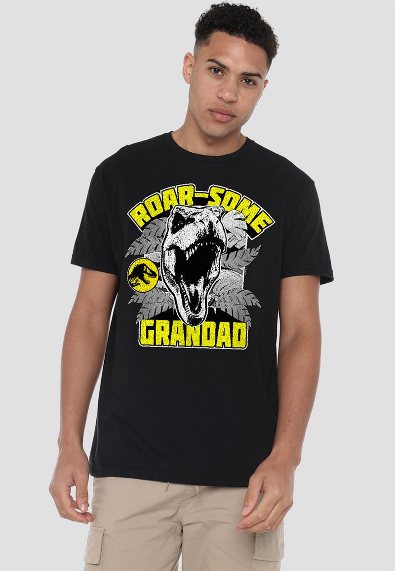 Black cotton t-shirt featuring a large graphic of a dinosaur skull, green leaves, and the text "ROAR-SOME GRANDAD" in yellow and white.