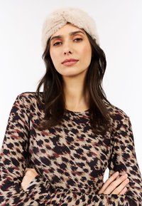 Cinta para la cabeza de piel sintética en beige claro, con una textura gruesa y suave. Parte superior estampada en tonos terrosos con un diseño abstracto.