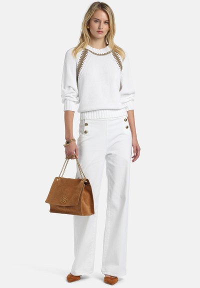 Pulover alb tricotat cu accente aurii, asortat cu pantaloni albi cu talie înaltă prevăzuți cu nasturi. Geantă maro din piele întoarsă și pantofi asortați.