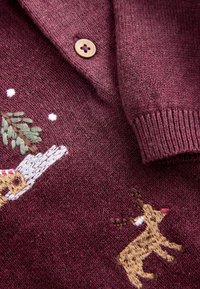 Bordeaux gebreide trui met borduursels van een rendier en een boom, met eenbruine knop en geribde manchetten. Zachte textuur en gedetailleerde patronen.