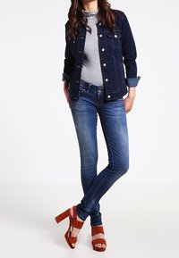 Mörk denimjacka, grått polotröja, blå skinny jeans och bruna högklackade sandaler, som framhäver olika material och texturer.