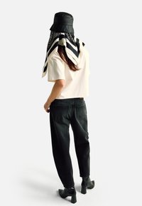 Černý klobouk typu bucket, krémový krátký top, tmavé džínsy s vysokým pasem a černé kotníkové boty na podpatku; šátek s geometrickým vzorem přehoděný přes ramena.