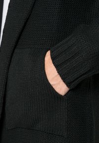 Svart texturerad kavaj med ribbade manschetter och sidofickor. Tyget har ett vävt utseende som ger djup till designen.