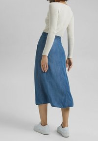 Jeanskjol i A-linje, midjelång, blå, med en slät textur. Har en sydd midjeresår och en detalj med sidoseam, kombinerad med vita sneakers.