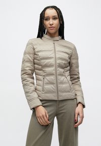 Smėlio spalvos minkšta dygsniuota striukė su užtrauktuku ir aukštu apykakliu, turinti šonines kišenes ir lygų paviršių. Audinys turi subtilų raštuotą detalių.