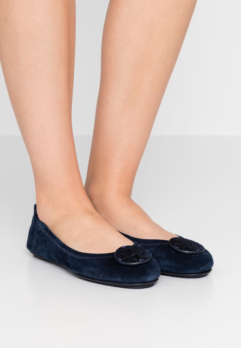 Des ballerines en suede bleu marine avec des accents noirs ronds sur le bout, des coutures visibles le long du bord et une texture douce.