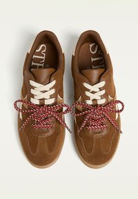 Sneakers in suede marrone con lacci bianchi e rossi a motivo annodati a fiocco, caratterizzati da accenti beige e suole testurizzate.