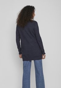 Marineblauer Langarmstrickpullover mit lockerer Passform und gerippten Bündchen, kombiniert mit weiten Jeanshosen aus hellem Denim. Weiche Textur und mittellanges Design.