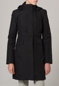 Manteau noir imperméable avec un col haut, une capuche ajustable, deux poches avant et une silhouette cintrée. Présente une texture lisse et un design minimaliste.
