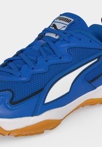 Μπλε αθλητικό παπούτσι Puma με λευκό και μαύρο λογότυπο, επάνω μέρος από δίχτυ, μπλε κορδόνια και πορτοκαλί λαστιχένια σόλα ορατά σε λευκό φόντο.